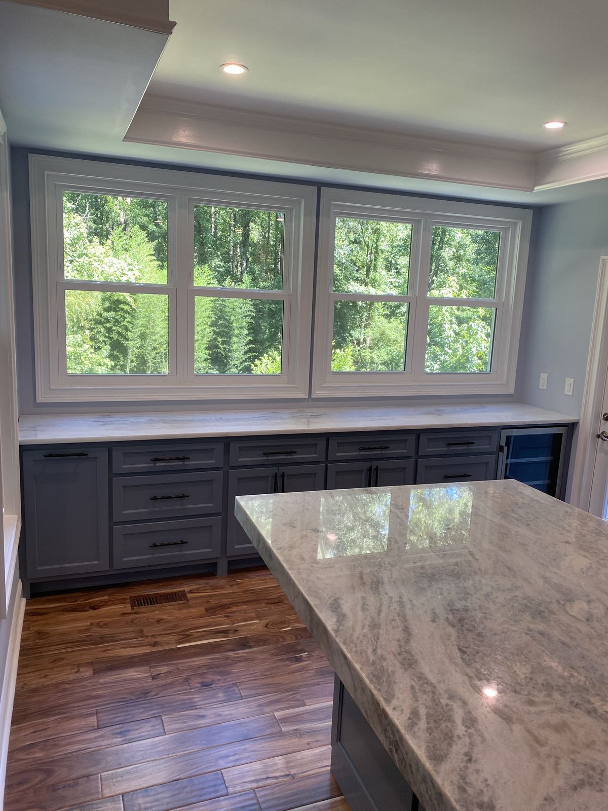 Grey shaker base cabinets with black pulls under a white quartzite countertop along a wall of windows