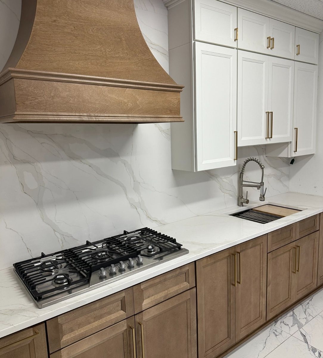 Close view of the Lanier Tawny range wall with a wood hood, Pearl White uppers, and a marble-look slab backsplash