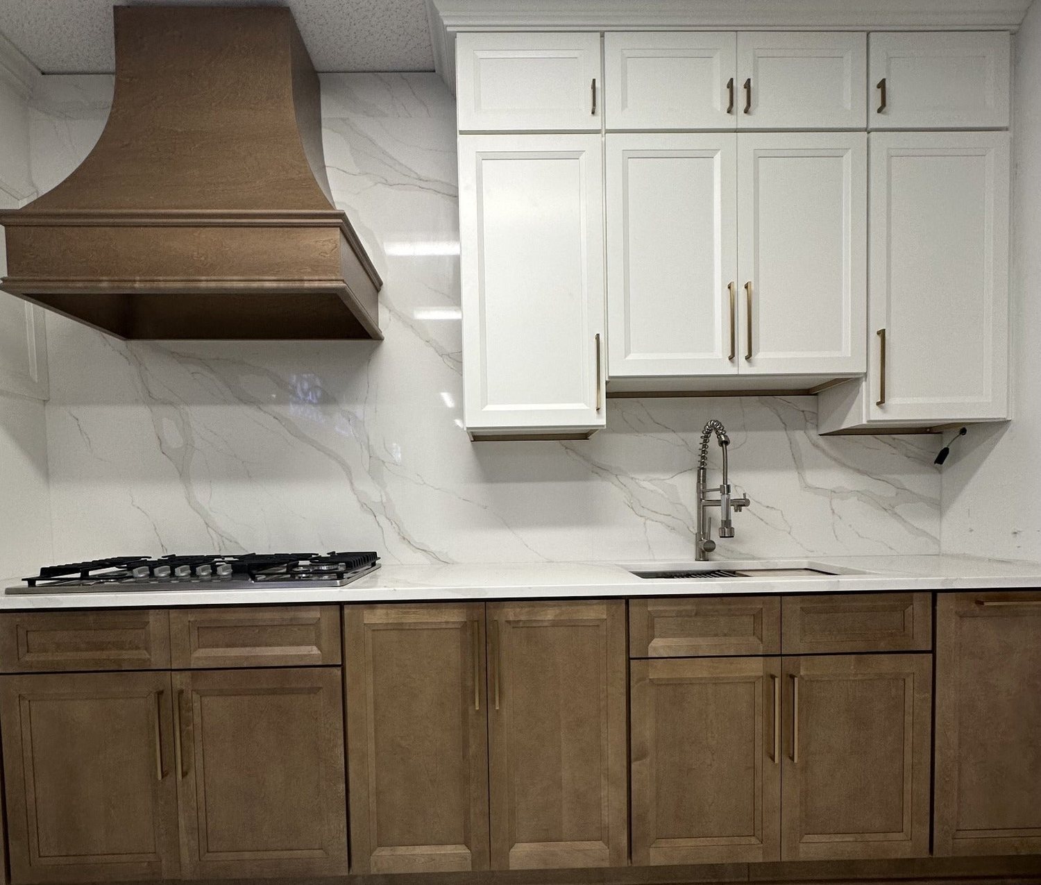 Kitchen with Lanier Pearl White upper cabinets, Lanier Tawny base cabinets, a wood range hood, and a marble-look slab backsplash